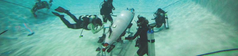 People in scuba gear swimming underwater and analyzing a small submarine.